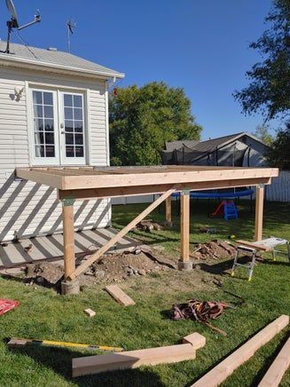 A wooden deck under construction attached to a white house with French doors, in a backyard.