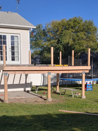 Partially built wooden deck with posts and railing supports in a backyard.