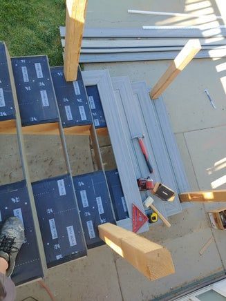 Staircase construction: grey composite decking being cut; tools visible, wooden supports, outside setting.