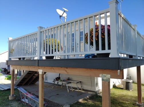 A gray and white elevated deck with railings and a stairwell, attached to a white house on a sunny day.