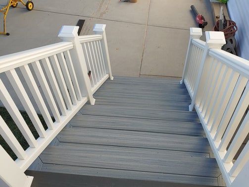Gray deck stairs with white railings leading down to a concrete patio.