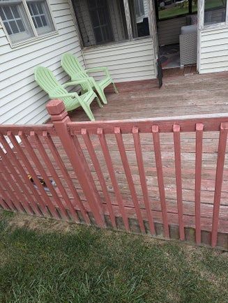 Red railing surrounds a weathered wooden deck with green chairs.