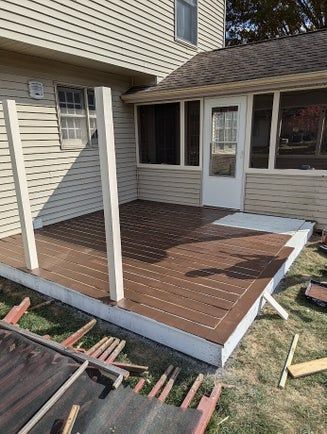 Partially built brown deck next to a house with a screened porch and white posts.