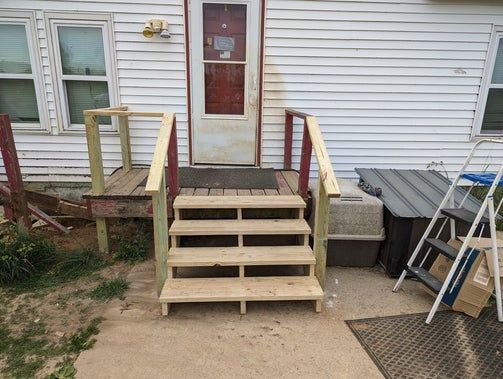 Wooden steps leading to a house's back door, with a small porch and handrails.