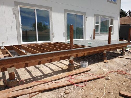 Partially built wooden deck against a white house with sliding glass doors.