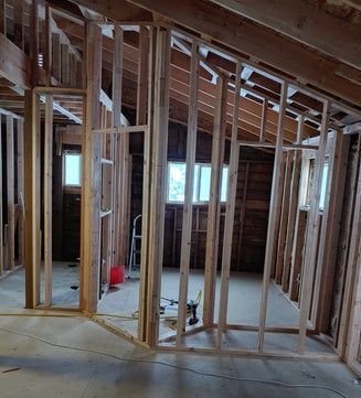 Wooden framing of a room, with windows and door openings, under construction.