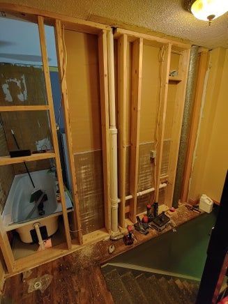 Bathroom renovation: wall studs, plumbing, and tub exposed. Brown and tan tones, construction in progress.