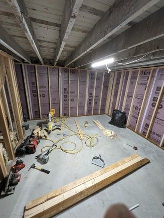 Basement renovation in progress with framed walls, insulation, tools, and wooden beams.