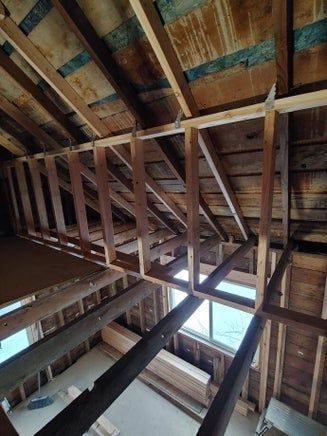 Wooden attic framework with support beams and bracing, daylight visible.