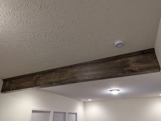 Wooden beam on a white ceiling, contrasted with light-colored walls. Smoke detector and recessed light visible.