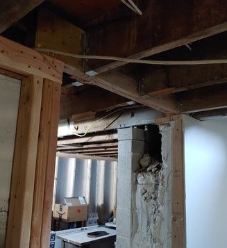 Basement framing with exposed joists, concrete block support, and electrical wiring. Interior view.
