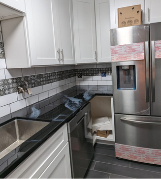Kitchen with white cabinets, black countertops, stainless steel appliances, and tile backsplash.