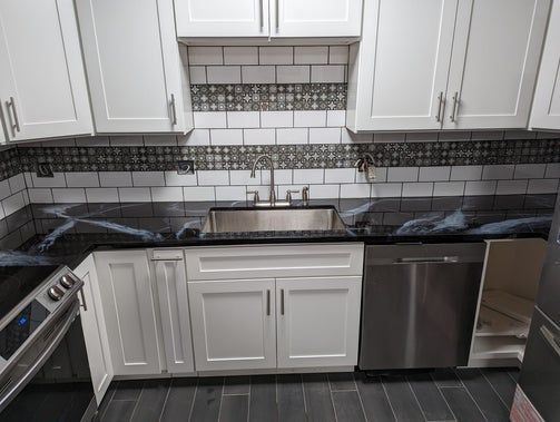 White kitchen cabinets with dark countertops, stainless steel sink, and backsplash.