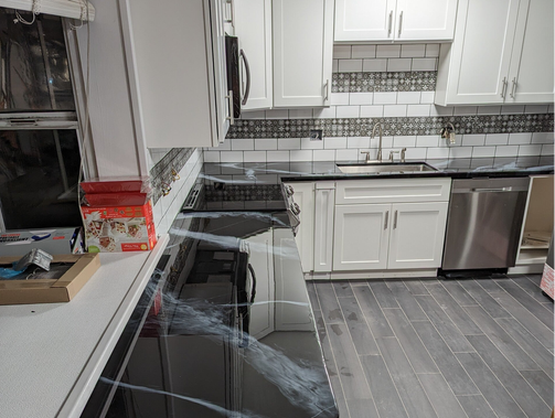 Kitchen with white cabinets, black countertops, stainless steel appliances, and gray flooring.