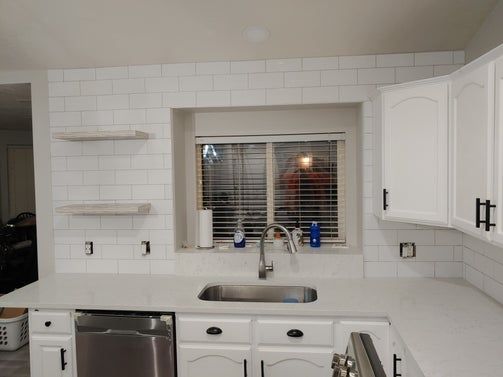 Kitchen with white cabinets, tiled backsplash, stainless steel sink, and window.