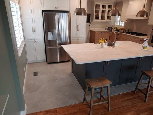 Modern kitchen: stainless steel fridge, navy island with white countertop, wood stools, light tile floor.