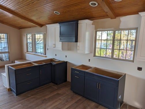 Kitchen renovation in progress: blue and white cabinets, wood ceiling, two windows.