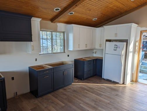 Newly renovated kitchen with white and blue cabinets, wood ceiling, and hardwood floor.