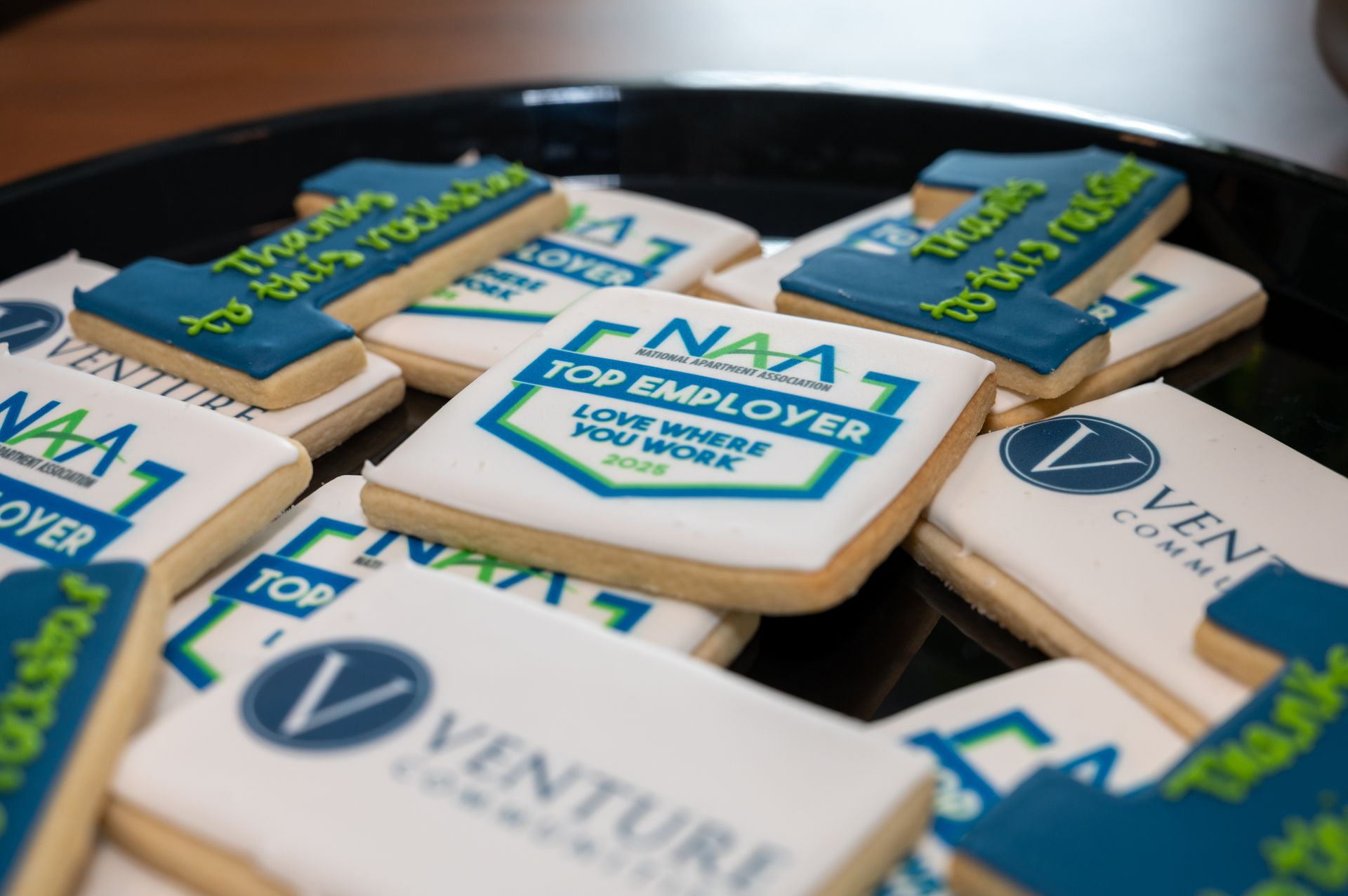 Decorated cookies featuring Venture Communities and NAA Top Employer logos arranged on a tray.