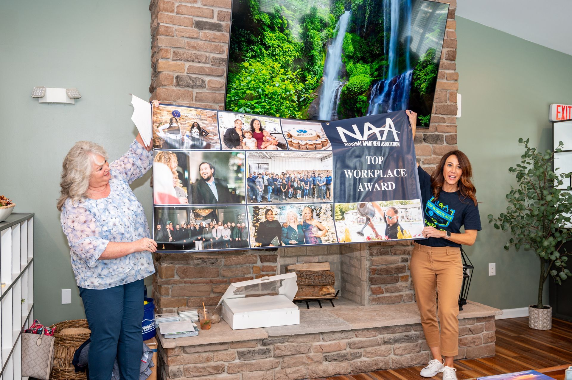 Two employees presenting an award poster with NAA Top Workplace recognition during a company event.