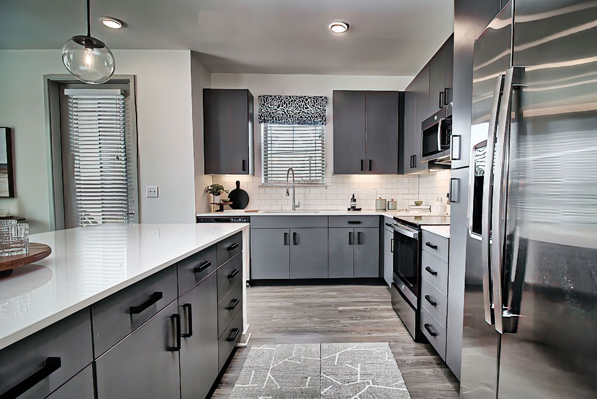 Modern kitchen with gray cabinets, white countertops, stainless steel appliances, and a window.