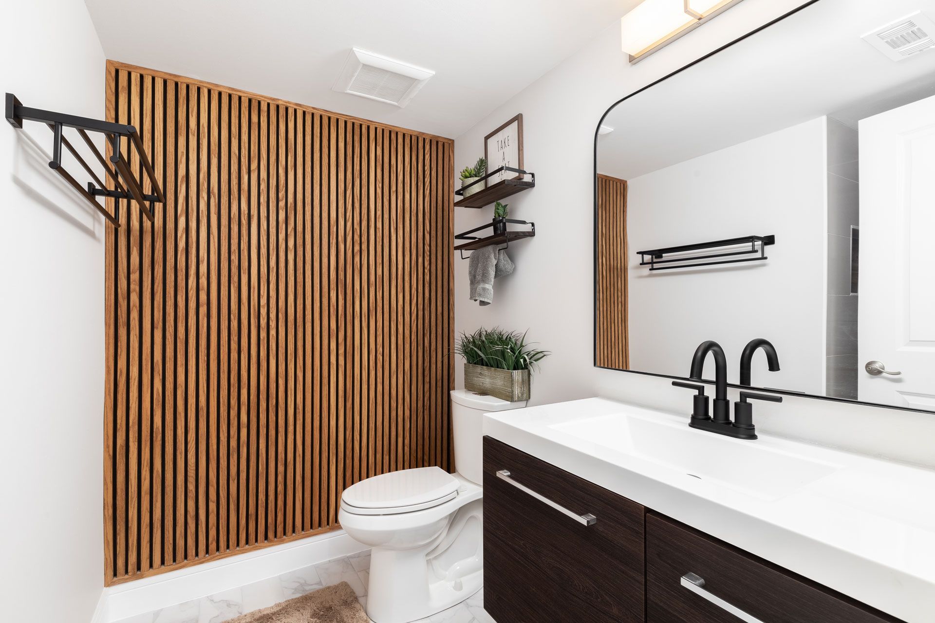 Modern bathroom with wood slat accent wall, floating shelves, and dark vanity.