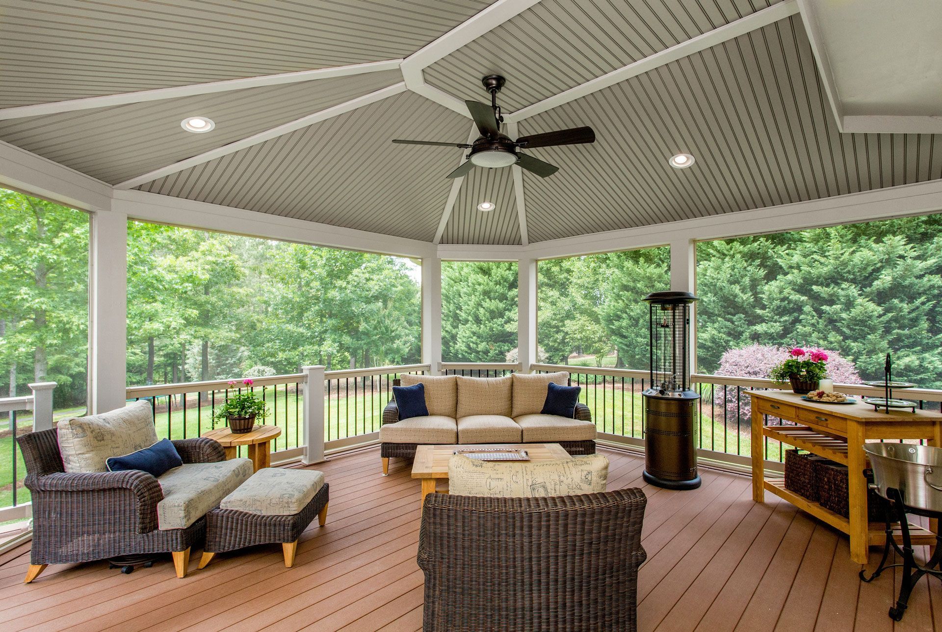 Screened-in porch with seating, ceiling fan, and heater, overlooking a wooded area.