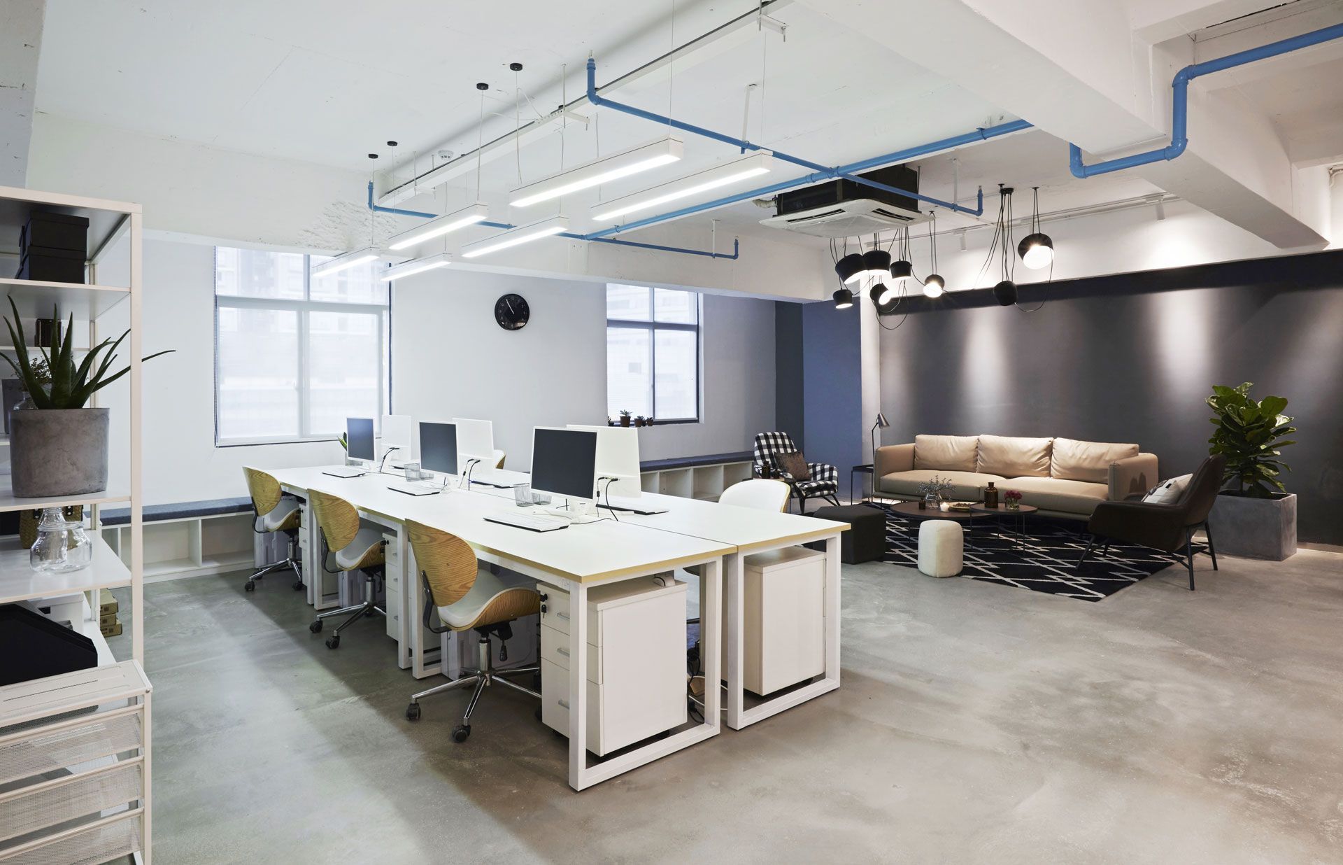 Modern office space with workstations, a lounge area, and a concrete floor.