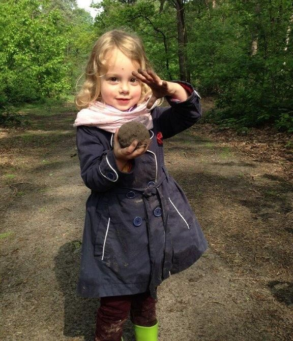 Een kind in een spijkerbroek en een vestje houdt ovenwanten vast en staat bij een speelkeukentje.