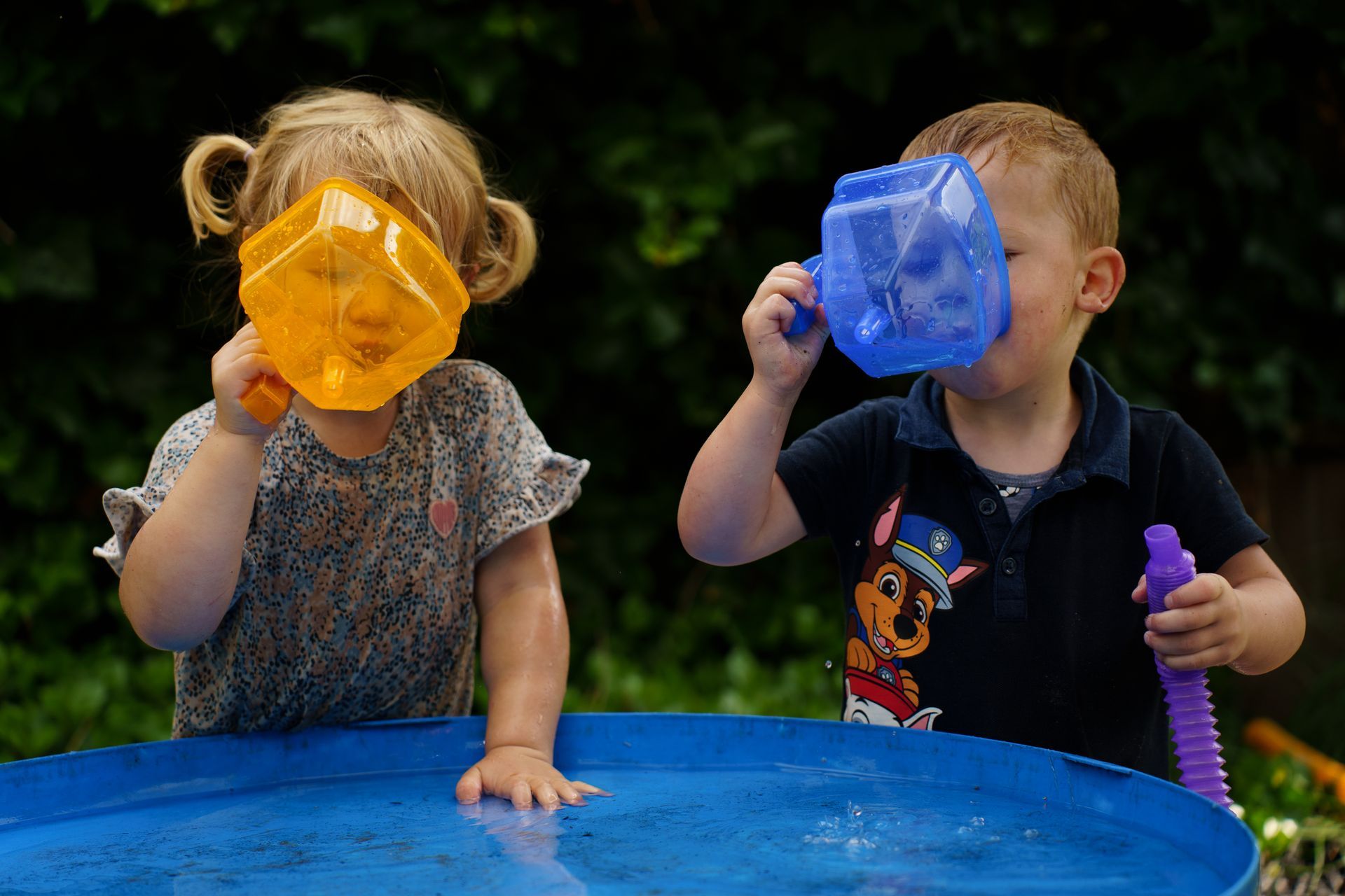 Een kind in een spijkerbroek en een vestje houdt ovenwanten vast en staat bij een speelkeukentje.