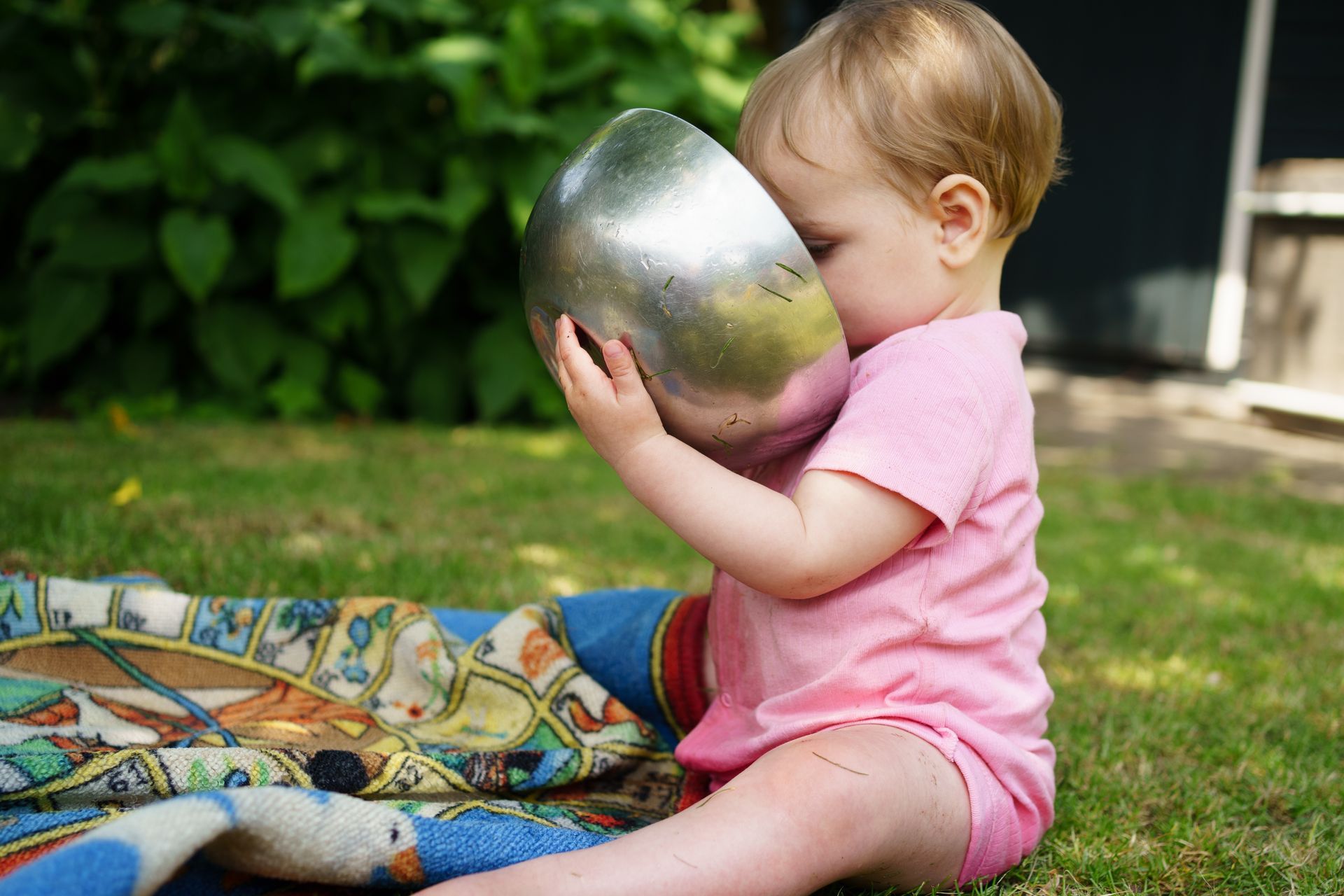 Een kind in een spijkerbroek en een vestje houdt ovenwanten vast en staat bij een speelkeukentje.