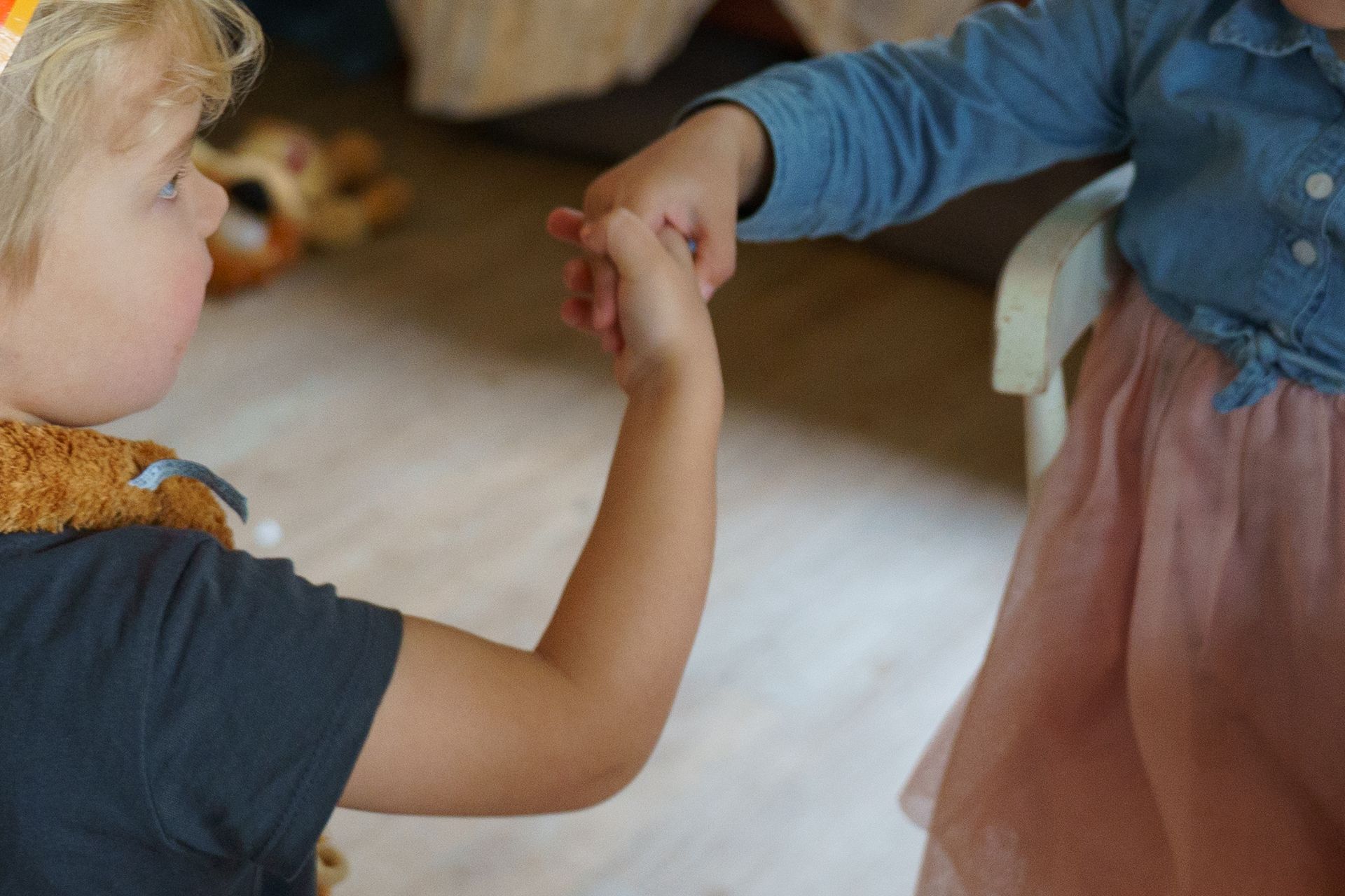 Een kind in een spijkerbroek en een vestje houdt ovenwanten vast en staat bij een speelkeukentje.