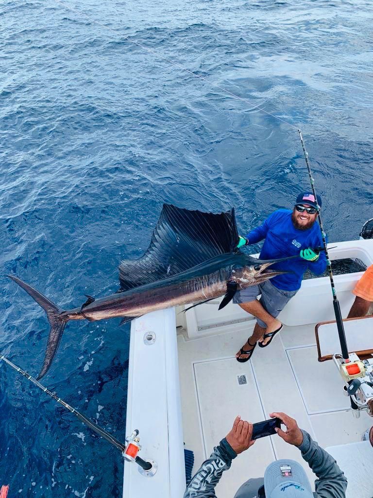 a man is sitting on a boat holding a sailfish .