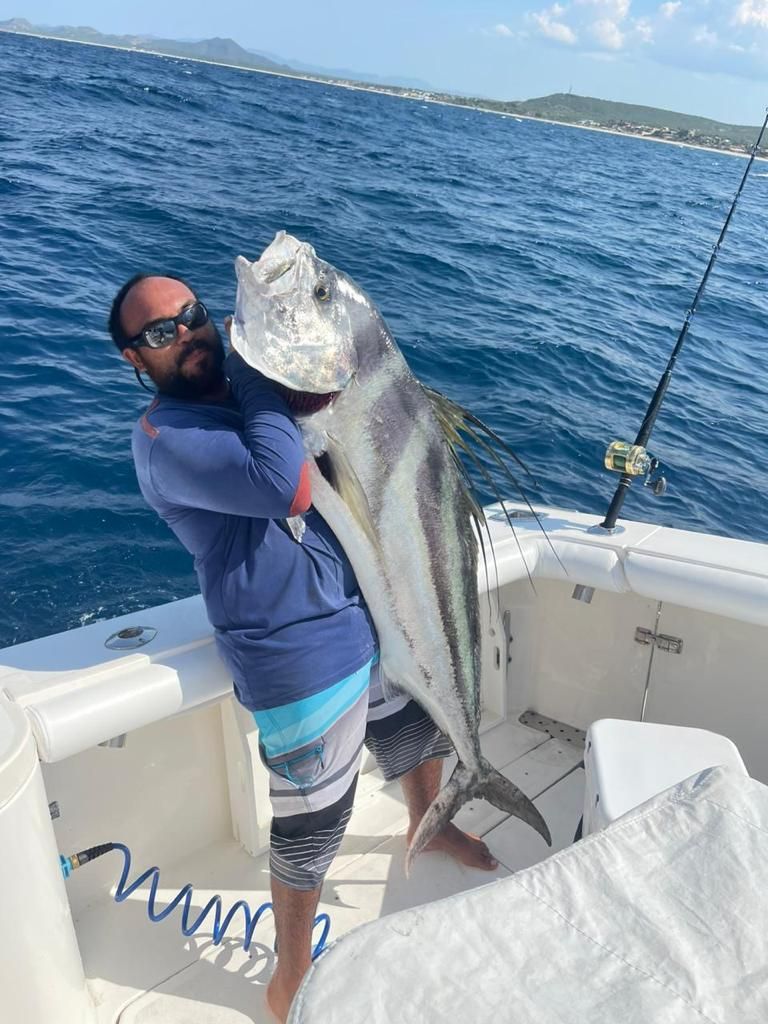 a man is holding a large fish on a boat in the ocean .