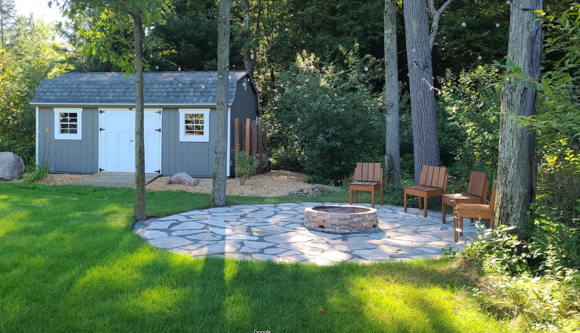 There is a fire pit in the middle of the yard in front of a shed.