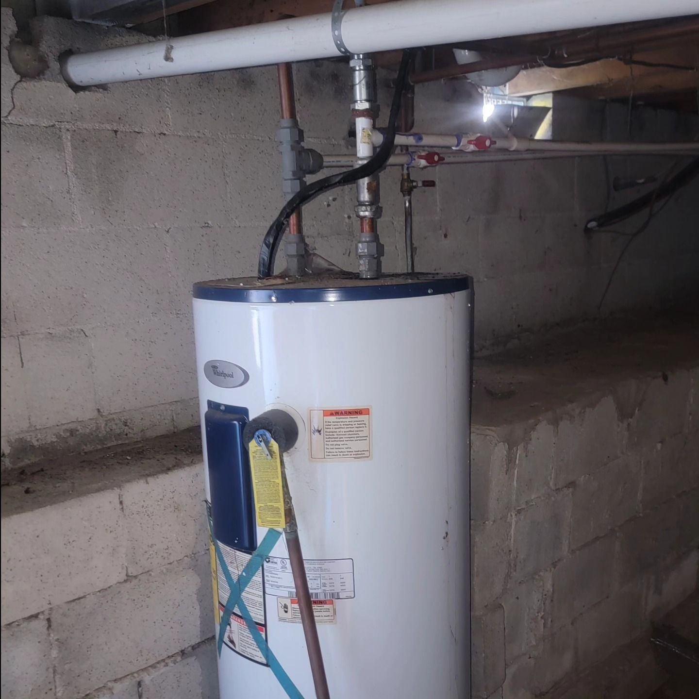 A white water heater is sitting under a brick wall