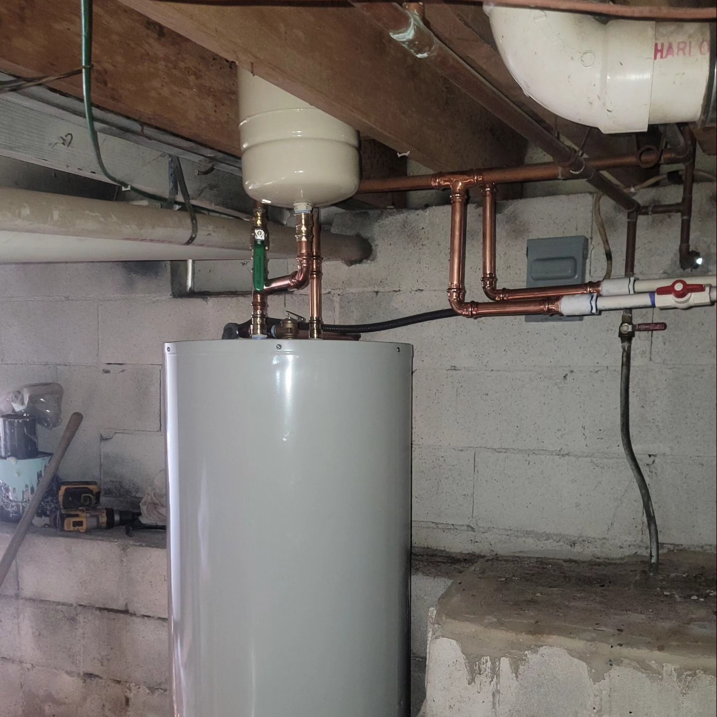 A white water heater in a basement with copper pipes
