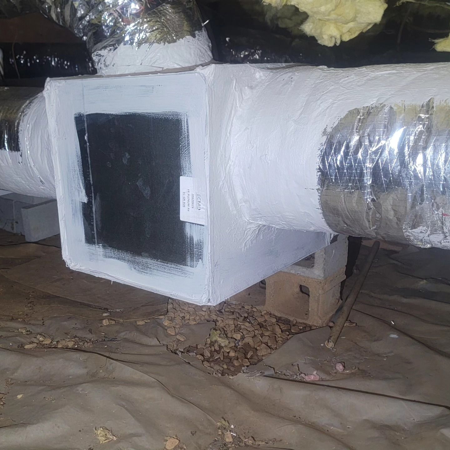 A white box is sitting on top of a metal pipe in a basement.