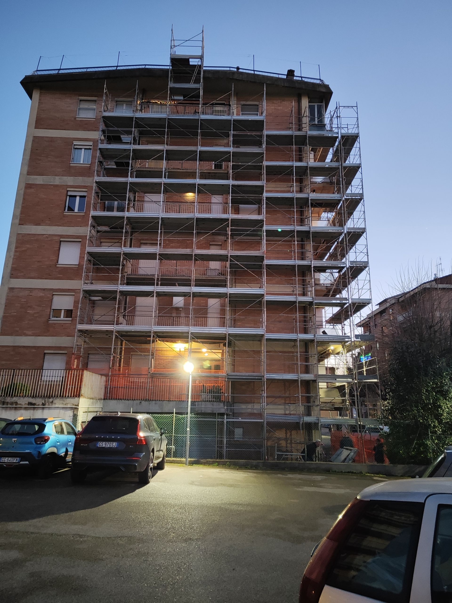 Edificio in fase di ristrutturazione con impalcature, auto parcheggiate e lampioni.