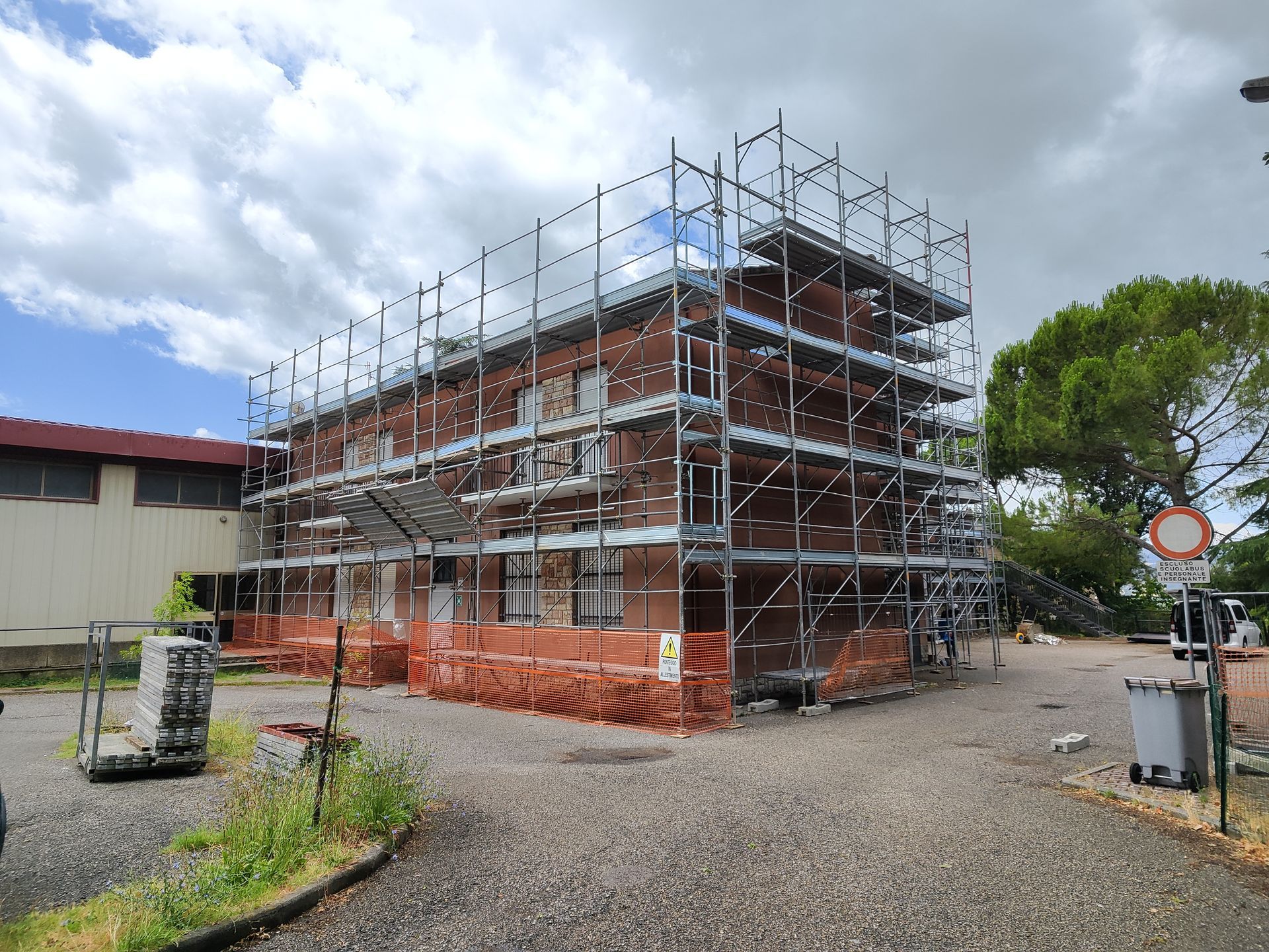 Edificio in mattoni in fase di ristrutturazione, circondato da impalcature. Cantiere in costruzione, cielo nuvoloso.