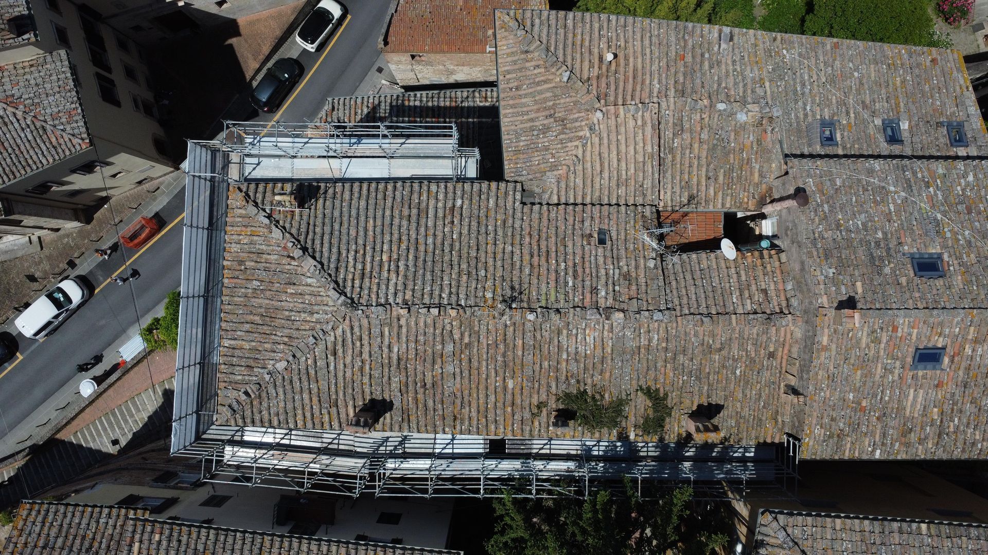 Vista dall'alto di vecchi tetti di tegole in un'area urbana. Tegole grigie, alcune danneggiate. Sono visibili la strada e le auto.