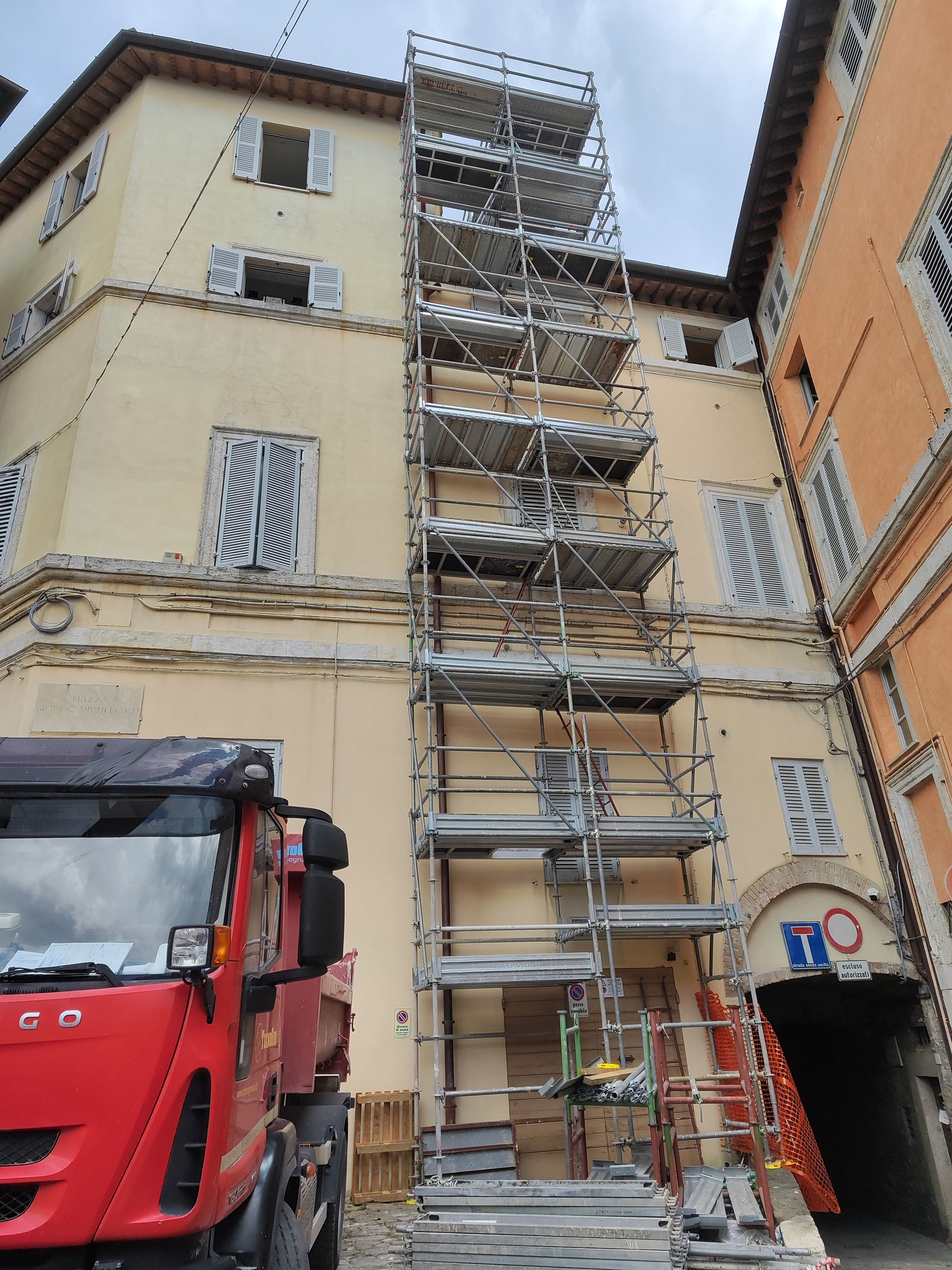 Impalcatura all'esterno dell'edificio accanto al camion rosso; edificio giallo con finestre chiuse.
