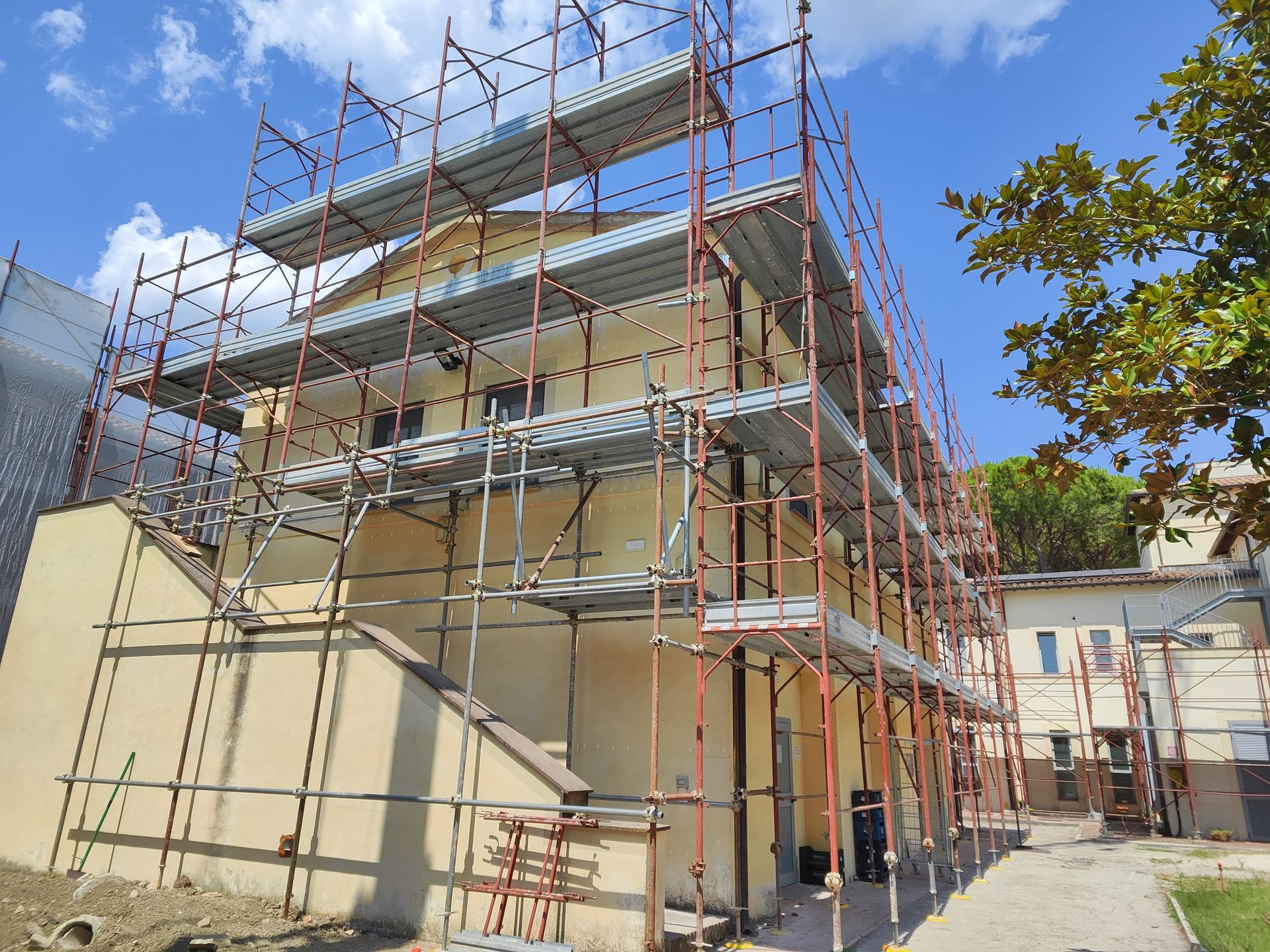 Un'impalcatura circonda un edificio giallo chiaro sotto un cielo azzurro, a indicare lavori di costruzione o ristrutturazione.