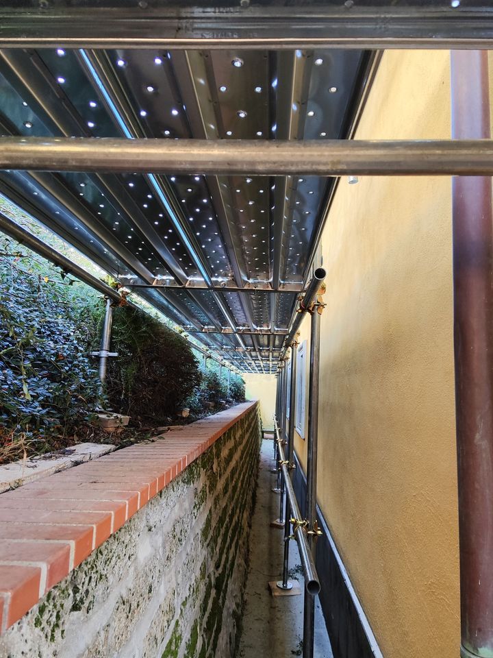 Impalcature lungo uno stretto sentiero tra un muro di mattoni e un edificio giallo.