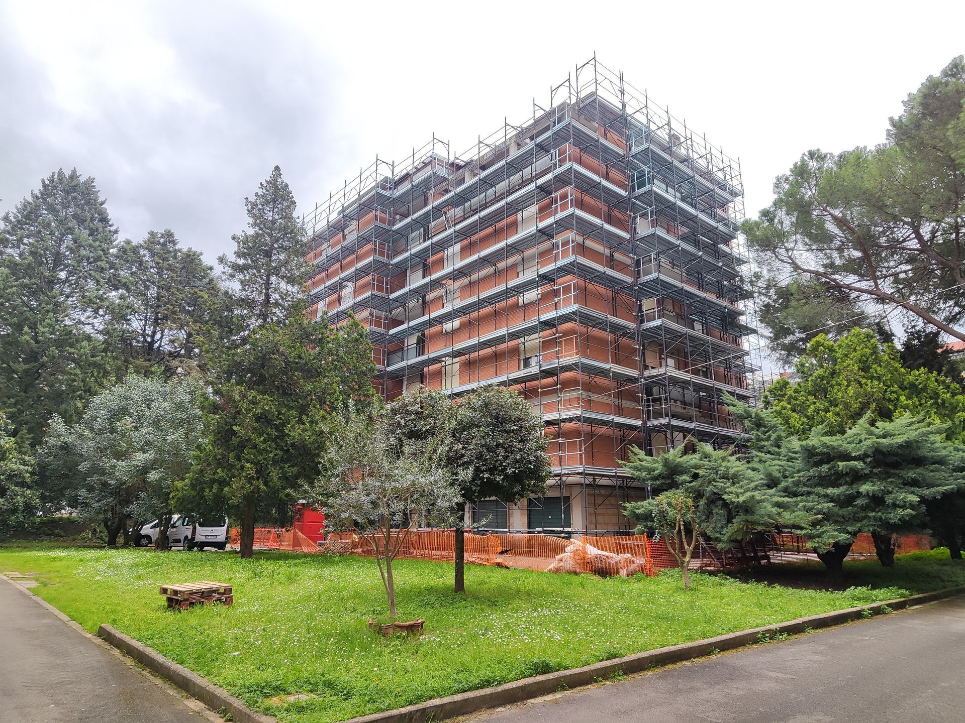 Edificio in costruzione; facciata in mattoni con impalcature, circondato da alberi ed erba.