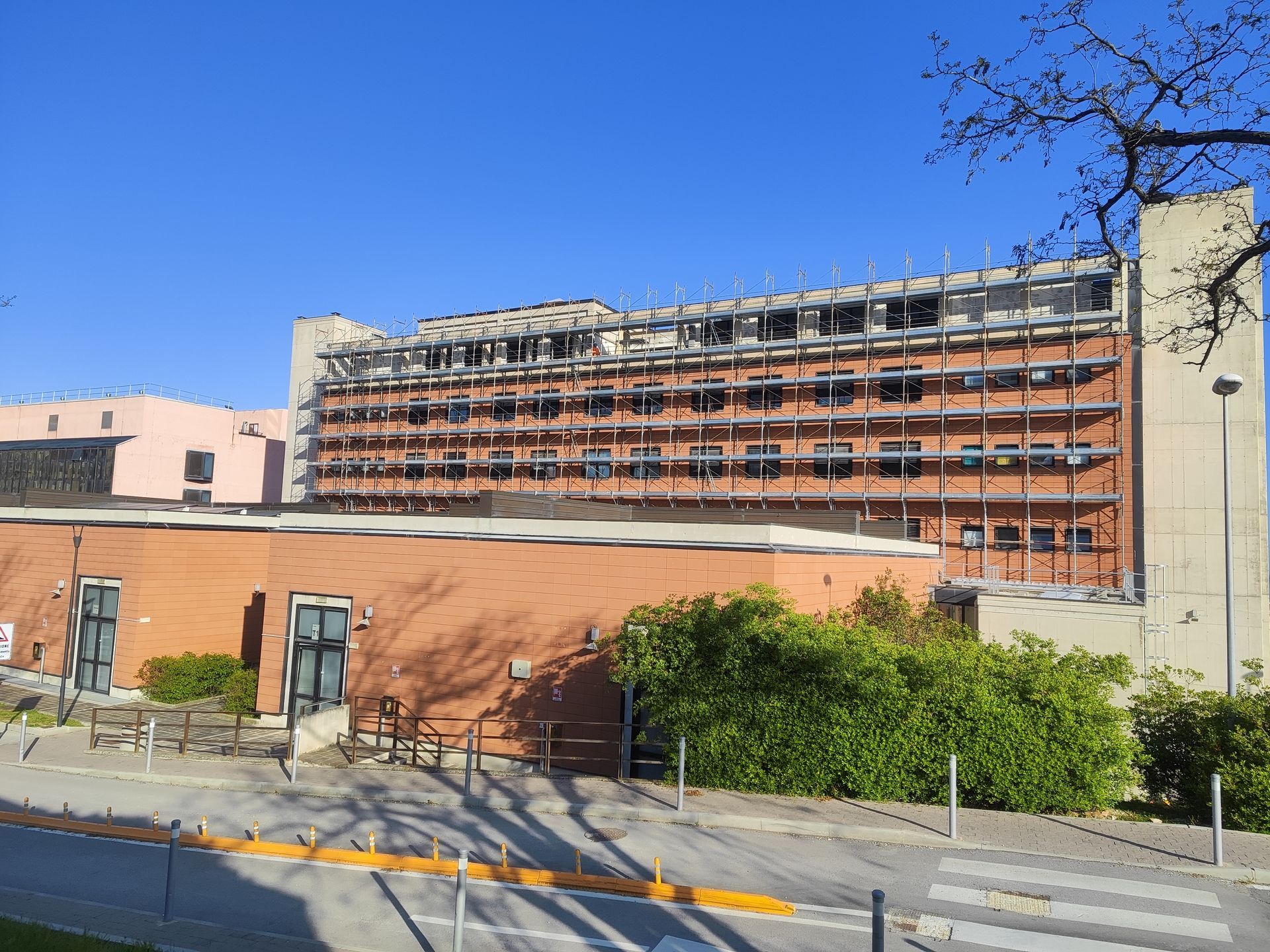 Edificio ospedaliero con facciata in mattoni a più piani sotto un cielo azzurro.