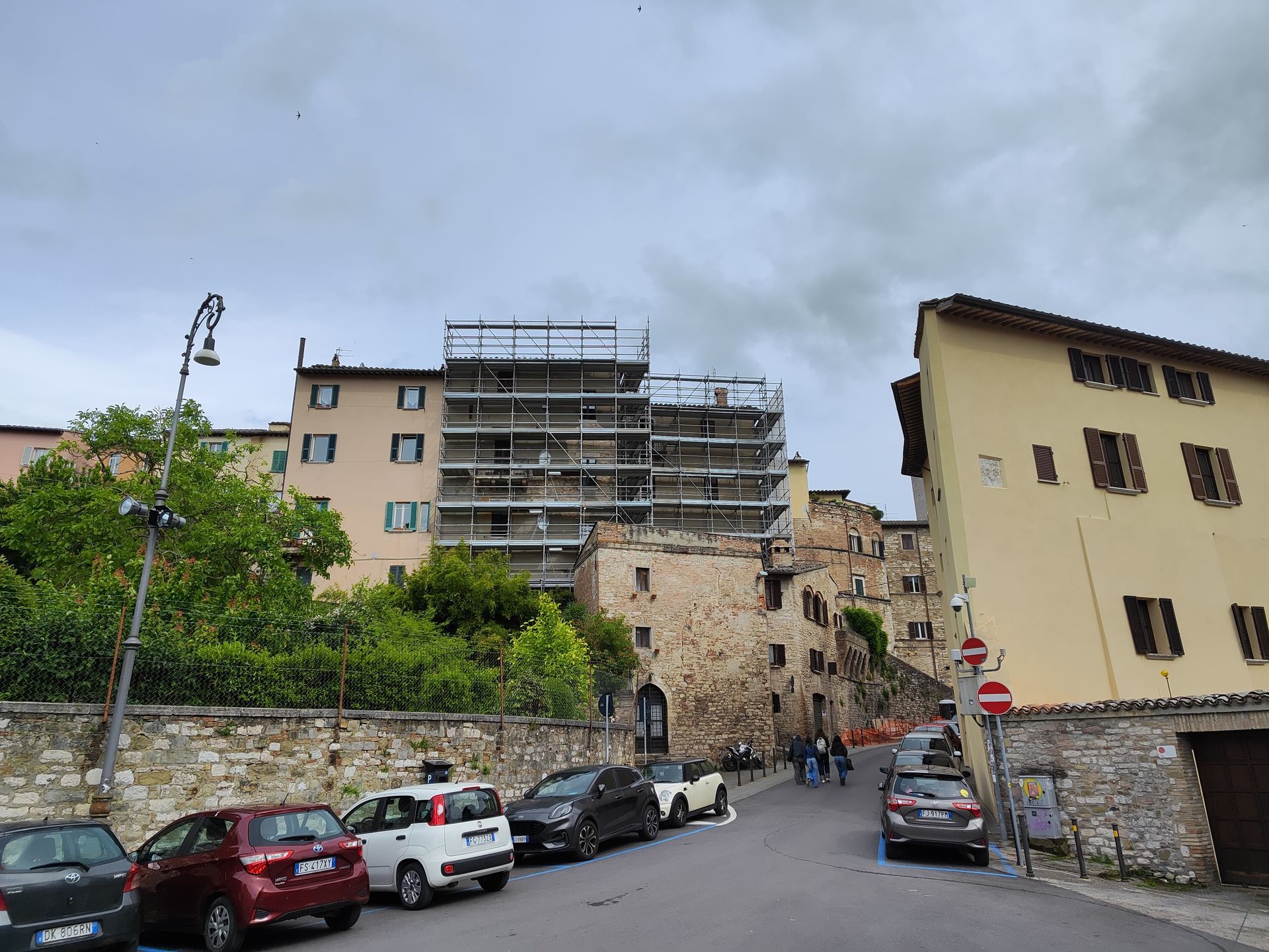 Scena di strada in Italia con auto parcheggiate, edifici, impalcature e cielo nuvoloso.
