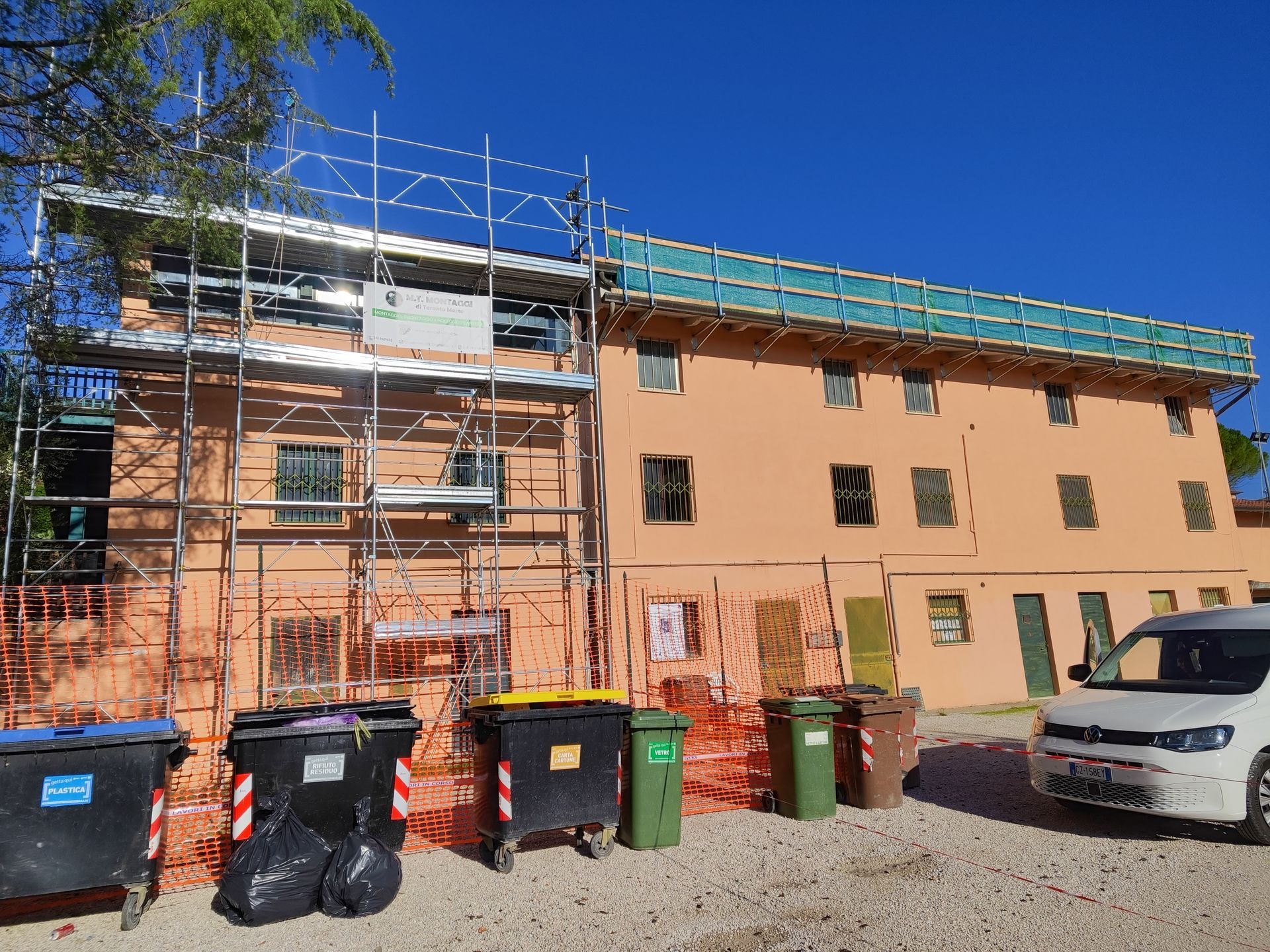Edificio in costruzione con impalcature e bidoni della spazzatura di fronte.
