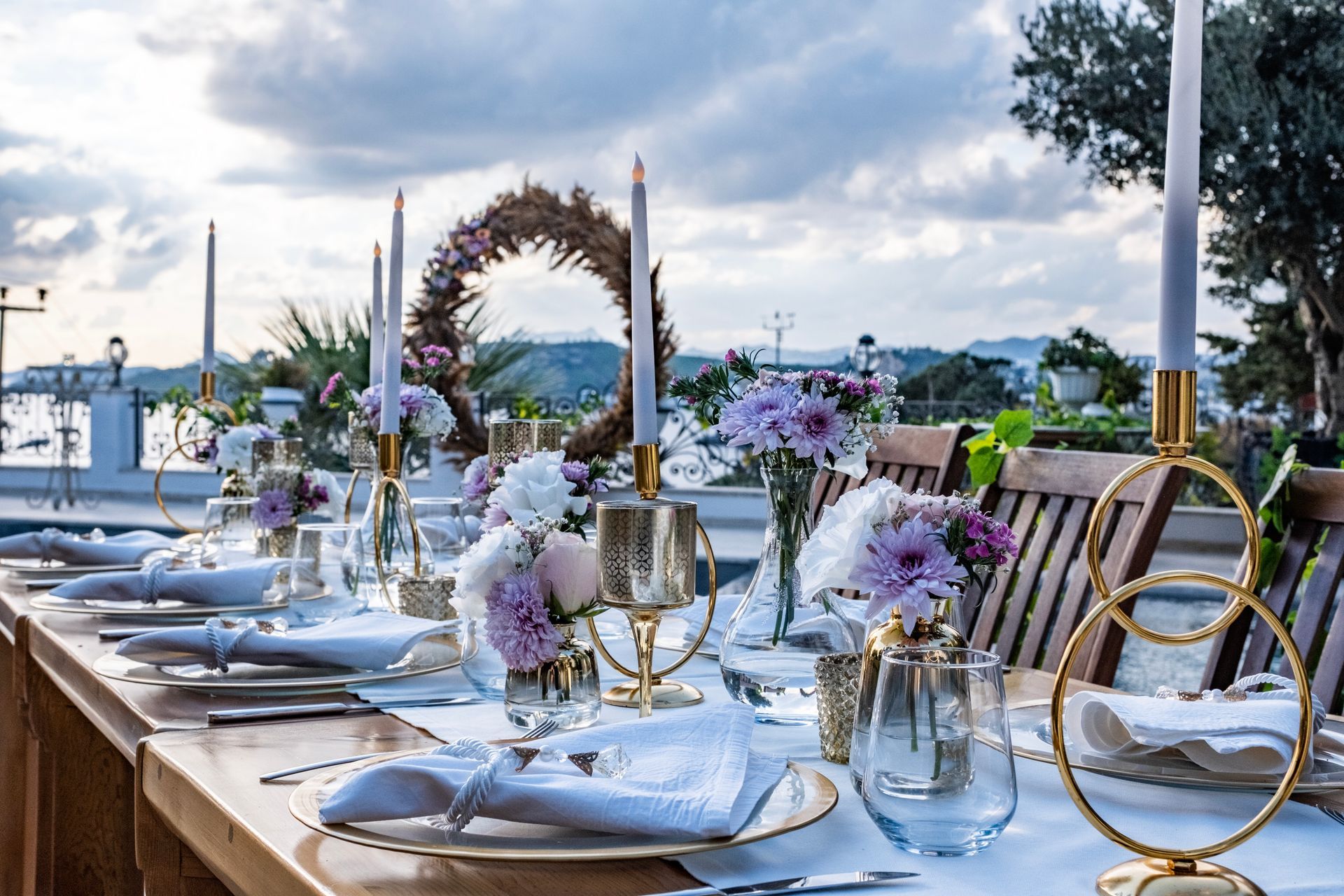 A long wooden table with plates , glasses , candles and flowers on it.