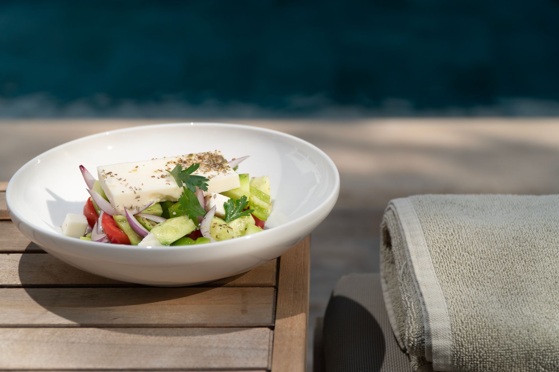 A bowl of salad is sitting on a wooden table next to a towel.
